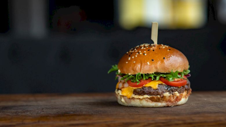 A delicious cheeseburger with lettuce, tomato, and sesame seed bun on a wooden surface, secured with a skewer on top.