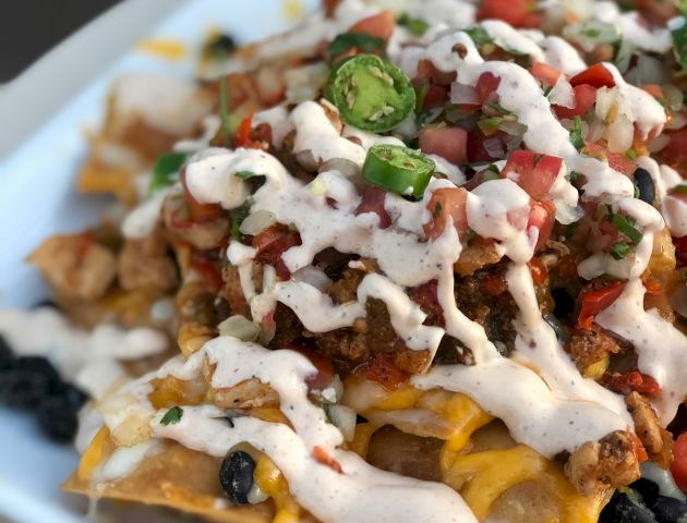 A plate of loaded nachos topped with cheese, diced tomatoes, jalapeños, black beans, and drizzled with a creamy sauce.