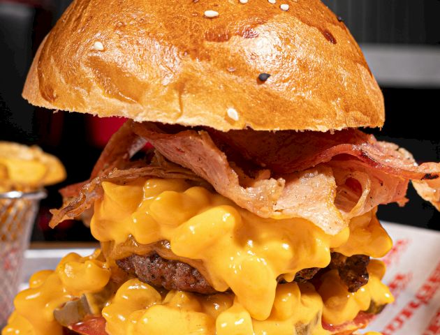 A burger topped with bacon, drenched in cheese sauce, and served in a sesame bun.