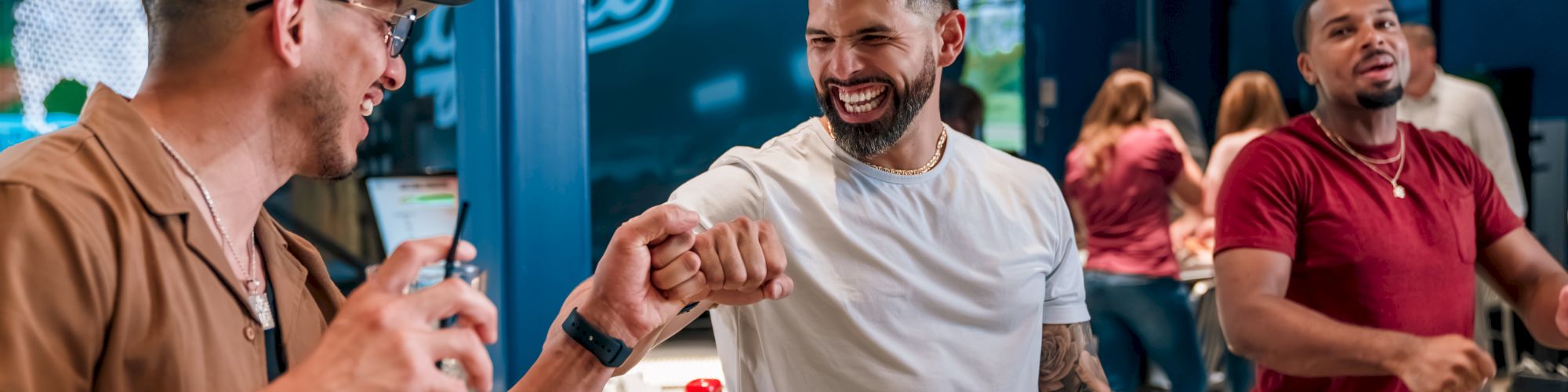 Three men are indoors having fun; two exchange a fist bump while the third smiles.