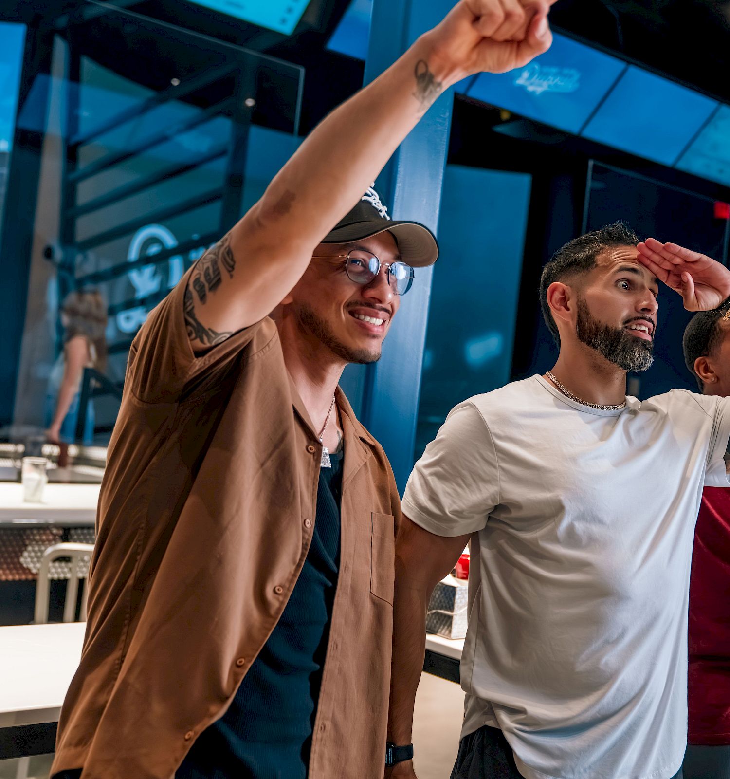 Three people standing indoors, two pointing and looking in a direction, appearing engaged or excited, with tables and screens around them.