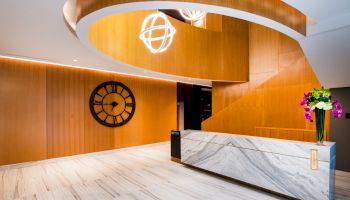 A modern interior with a marble reception desk, wooden walls, a large clock, spiral ceiling design, and decorative lights.