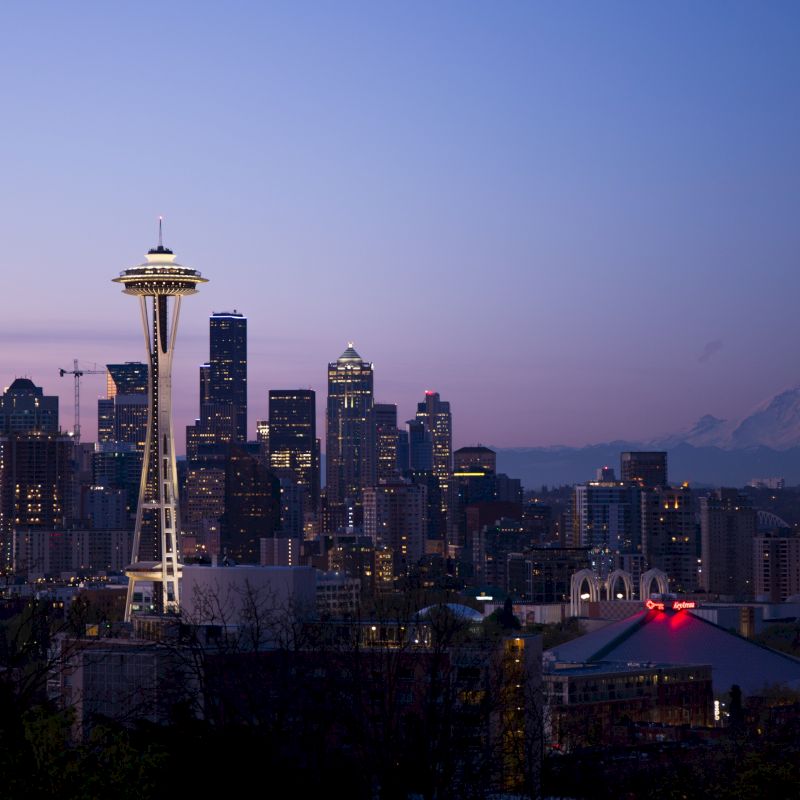 A twilight scene of Seattle with the Space Needle and Mount Rainier in the background, showcasing the city's skyline and evening ambiance.