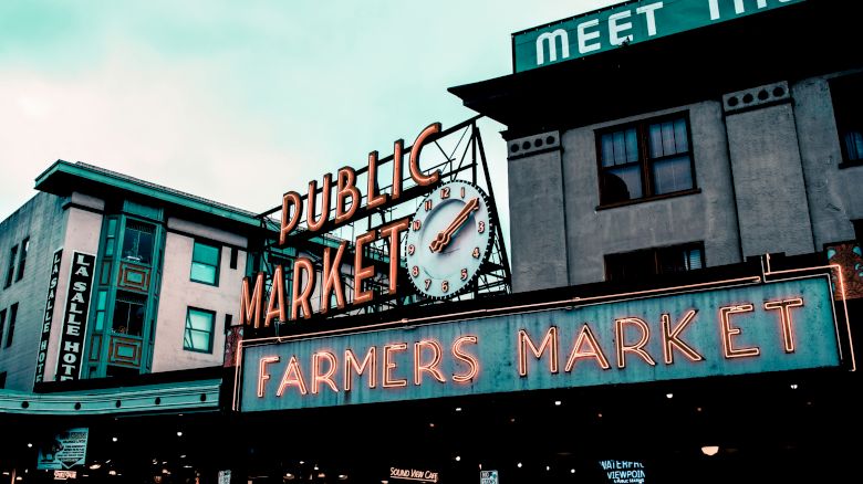 The image shows the iconic Public Market sign with a clock, and the Farmers Market sign at Pike Place Market in Seattle.